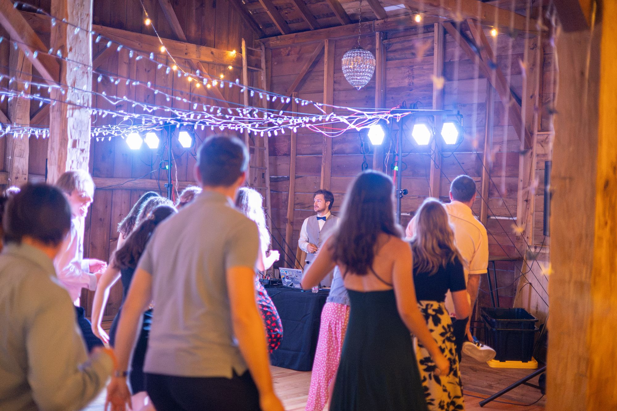 A packed barn dance floor under a canopy of string lights, with colour washes on the back wall